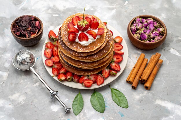 Een bovenaanzicht lekkere ronde pannenkoeken met roomkaneel en rode aardbeien op de lichte bureaucake