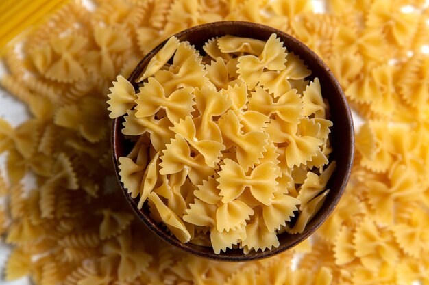 Een bovenaanzicht rauwe italiaanse deegwaren weinig gevormd met bruine plaat op de heldere bureau pasta Italiaans eten maaltijd