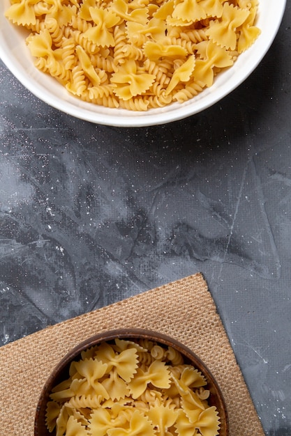 Een bovenaanzicht rauwe italiaanse pasta weinig gevormd binnen bruine en witte plaat op de grijze bureau pasta Italiaans eten maaltijd