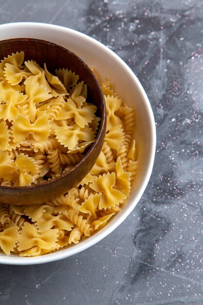 Een bovenaanzicht rauwe italiaanse pasta weinig gevormd binnen bruine en witte plaat op de grijze bureau pasta Italiaans eten maaltijd