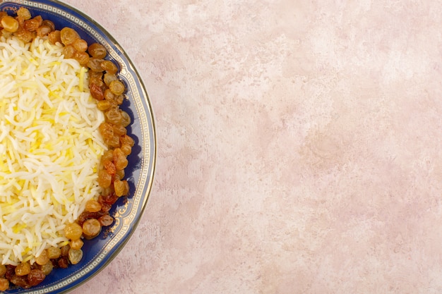 Gratis foto een bovenaanzicht smakelijke pilaf met olie en gedroogde rozijnen binnen plaat op het roze oppervlak