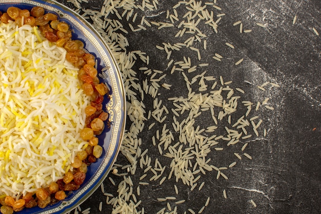 Een bovenaanzicht smakelijke pilaf met olie en gedroogde rozijnen in plaat met rauwe rijst op het donkere oppervlak