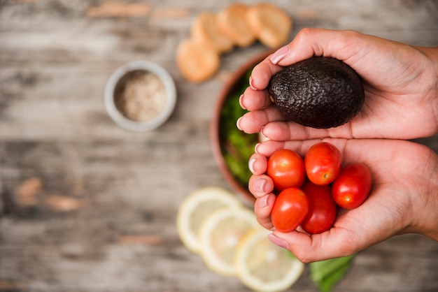 Een bovenaanzicht van cherrytomaatjes en avocado in handen op wazig houten bureau