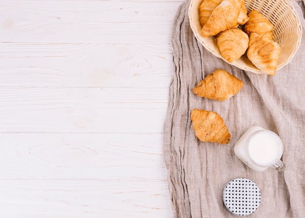 Een bovenaanzicht van croissants en melk in metselaar kruik op houten achtergrond