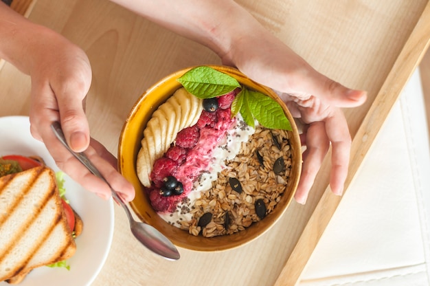 Een bovenaanzicht van de hand van de vrouw met kom van zelfgemaakte muesli op dien blad