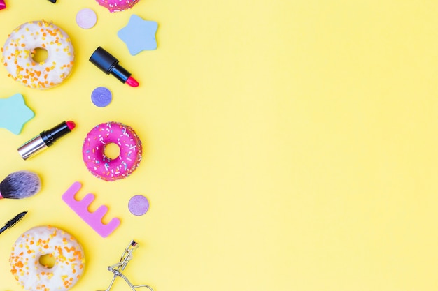 Een bovenaanzicht van donuts; lippenstift; wimperkruller; make-up borstel en teen divider op gele achtergrond