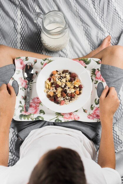 Een bovenaanzicht van een jongen zittend op bed met gekruiste been met gezonde haver maaltijd