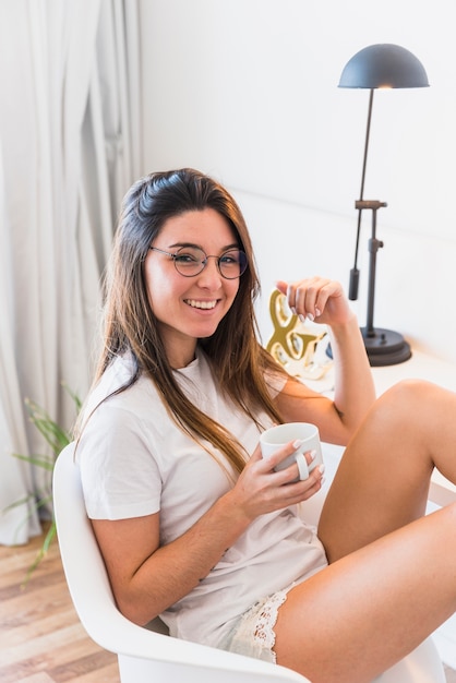 Een bovenaanzicht van een lachende jonge vrouw zittend op een stoel met koffiekopje