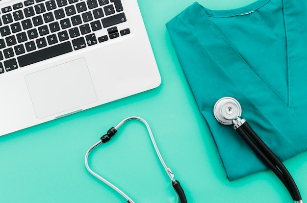 Een bovenaanzicht van een laptop; stethoscoop en medische uniform op groene achtergrond