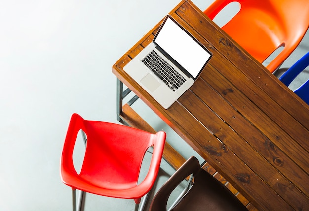 Een bovenaanzicht van een open laptop op houten tafel met kleurrijke stoelen