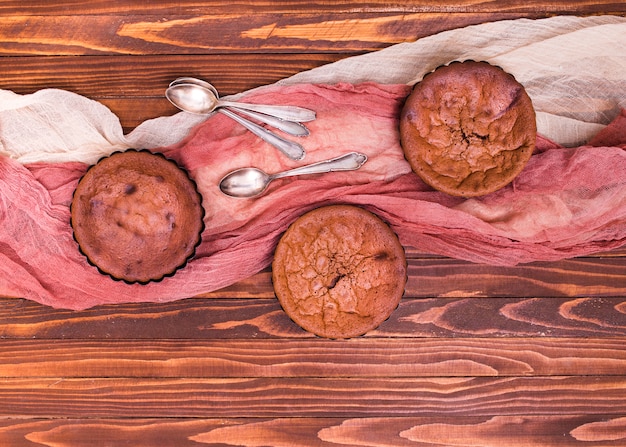 Een bovenaanzicht van gebakken chocolade cake met lepel en kleding op houten achtergrond