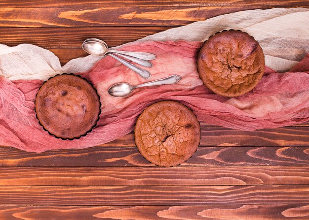 Een bovenaanzicht van gebakken chocolade cake met lepel en kleding op houten achtergrond