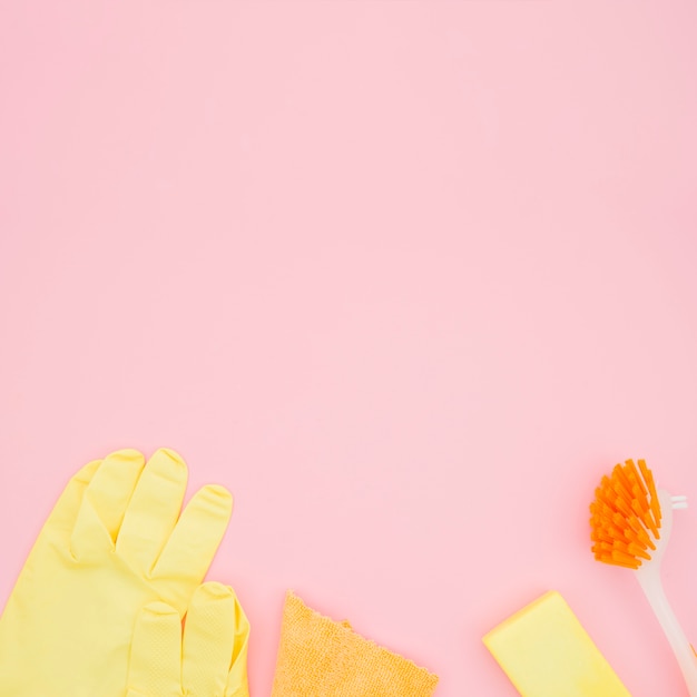 Een bovenaanzicht van handschoenen; borstel; spons en fles op roze achtergrond