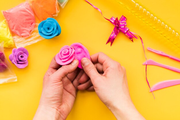 Een bovenaanzicht van iemands hand maken van de kleurrijke roze roos op gele achtergrond