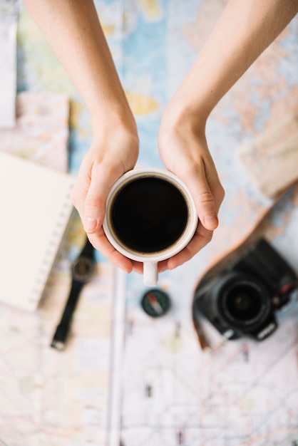 Een bovenaanzicht van iemands hand met koffiekopje over de wazig kaart