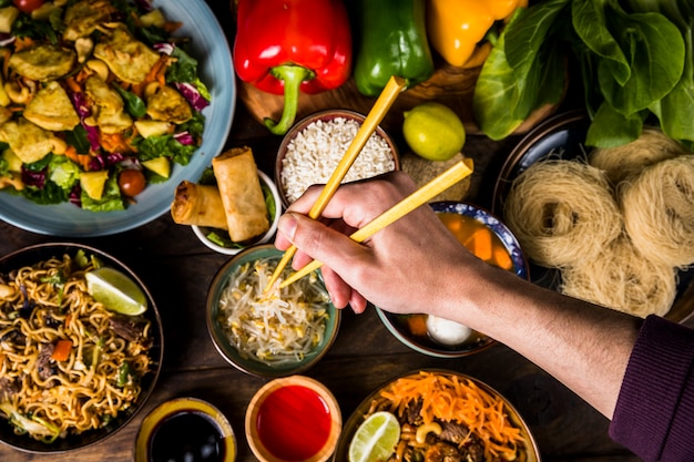 Een bovenaanzicht van iemands hand met stokjes over het heerlijke Thais eten