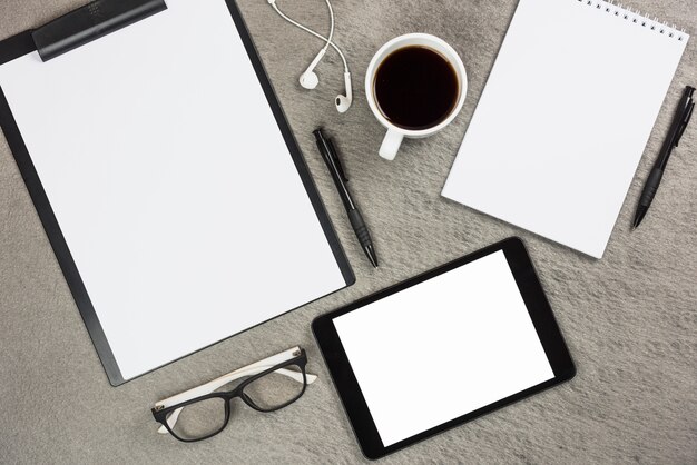 Een bovenaanzicht van kantoorbenodigdheden met koffiekopje en digitale tablet op grijs bureau