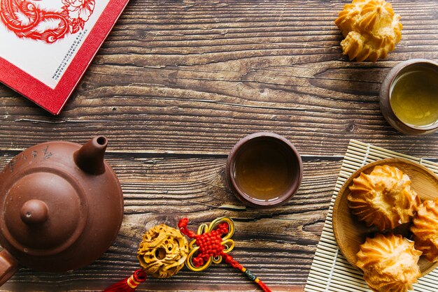 Een bovenaanzicht van kleitheepot en theekopjes met zelfgemaakte kokoskoekjes over de houten tafel