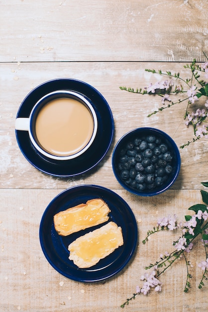 Gratis foto een bovenaanzicht van koffie; bosbessen; toast en bloemen op houten bureau