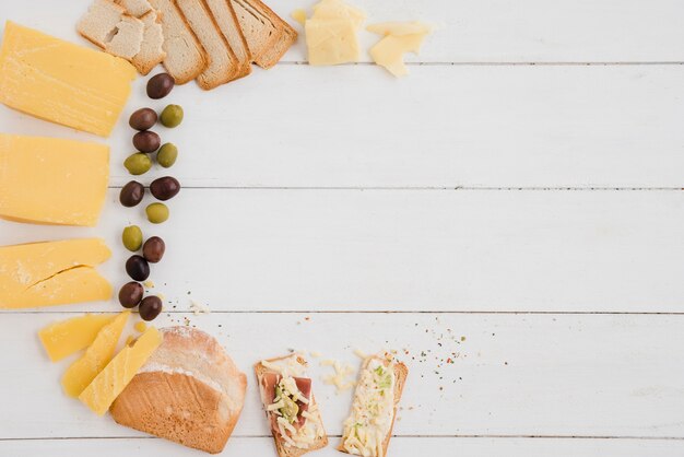 Een bovenaanzicht van olijven; kaas plak en brood op witte houten tafel