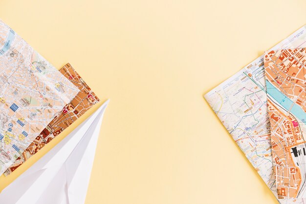 Een bovenaanzicht van steden wegenkaarten en papieren vliegtuigje op gekleurde achtergrond