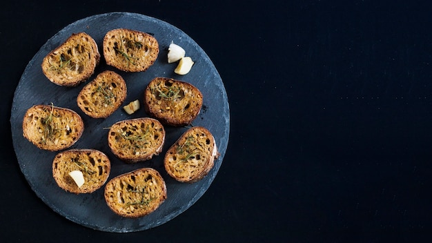 Een bovenaanzicht van toast met rozemarijn toppings op ronde leisteen tegen zwarte achtergrond