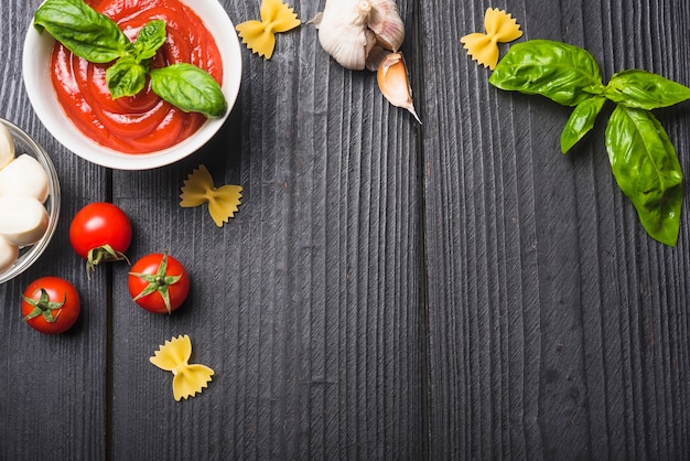 Een bovenaanzicht van tomatensaus met mozzarella; pasta; knoflook een basilicum op houten plank