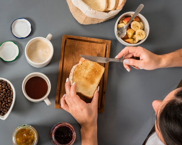 Een bovenaanzicht van vrouw die jam op brood met botermes op grijze achtergrond toepassen