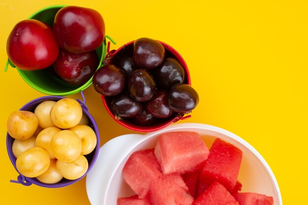Een bovenaanzicht vers fruit zoals gele en rode kersen, pruimen en watermeloen op geel, fruit zomerkleur