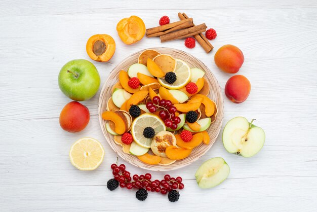 Een bovenaanzicht vers gesneden fruit kleurrijk en rijp met hele vruchten op het houten bureau en witte achtergrond fruit kleur voedsel foto