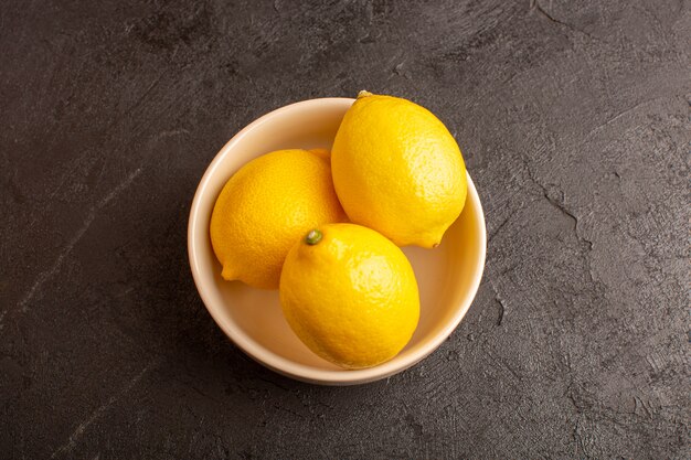 Een bovenaanzicht verse citroenen zuur rijp binnen witte plaat hele zachte citrus tropische vitamine geel op het donkere bureau