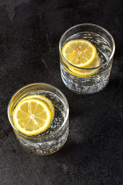 Een bovenaanzicht water met verse citroen koel drankje met gesneden citroenen in transparante glazen op de donkere achtergrond cocktail drinken fruit