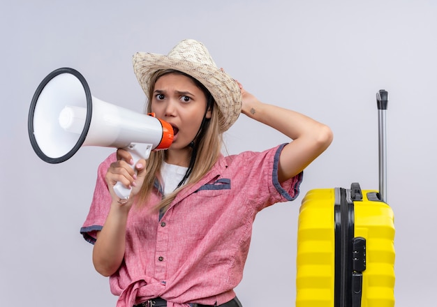 Gratis foto een boze jonge vrouw die rood overhemd en zonnehoed draagt die door megafoon met hand op hoofd spreken