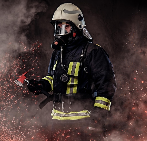 Een brandweerman gekleed in een uniform en een zuurstofmasker houdt een rode bijl vast die in vuurvonken staat en rook op een donkere achtergrond.
