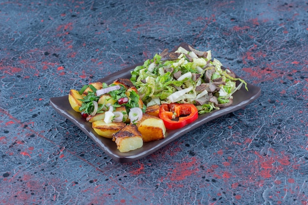 Een bruin bord groentesalade en gebakken aardappel.