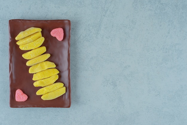 Een bruin bord met banaanvormige kauwsnoepjes met hartvormige zoete gelei-snoepjes