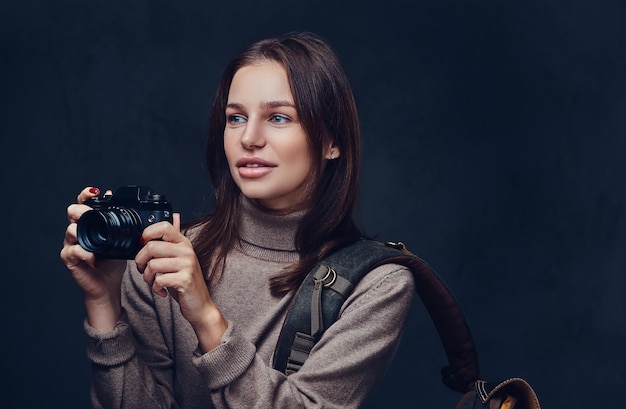 Een brunette vrouwelijke reiziger met rugzak houdt een compacte fotocamera vast.