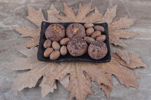 Een bundel koekjes en pecannoten op een schaal en een bos platanenbladeren op marmer