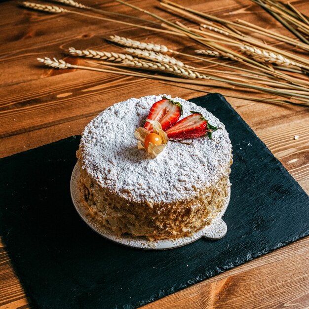 Een cake van de vooraanzichtroom verfraaide met de heerlijke cake van de aardbeien heerlijke verjaardag binnen witte de zoetheidsverjaardag van plaatbakkerij op de bruine achtergrond