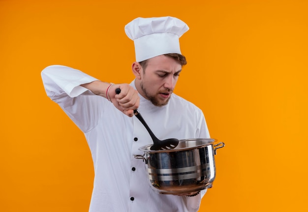 Een chef-kok man in wit uniform met zilveren roestvrijstalen kookpan met schuimspaan op een oranje muur