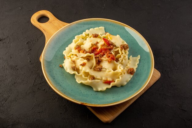 Een deeg pasta van bovenaanzicht gekookt lekker gezouten binnen ronde groene plaat op een donker bureau