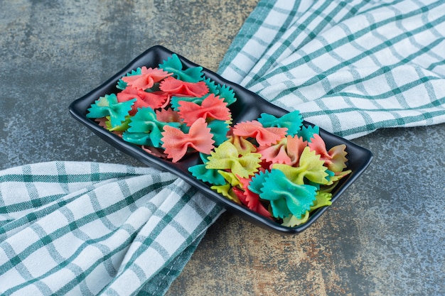 Een dienblad met kleurrijke farfalle-pasta's op de handdoek, op het marmeren oppervlak.