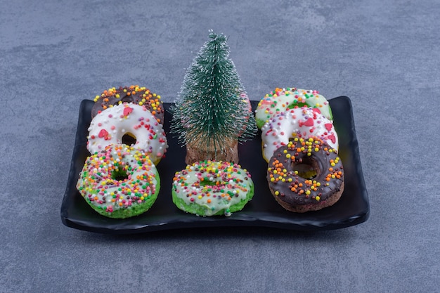 Een donker bord met heerlijke donuts en een kleine kerstboom