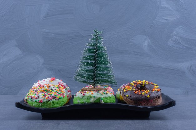 Een donker bord met heerlijke donuts en een kleine kerstboom