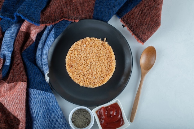 Een donker bord vol bulgur met peper en ketchup