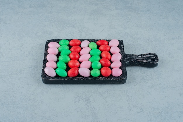 Gratis foto een donkere houten plank vol met ronde zoete kleurrijke snoepjes op een witte ondergrond