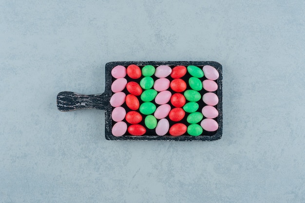 Gratis foto een donkere houten plank vol met ronde zoete kleurrijke snoepjes op een witte ondergrond