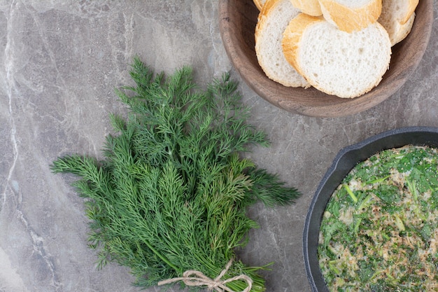 Gratis foto een donkere pan gebakken eieren met groenen en wit brood op marmeren achtergrond. hoge kwaliteit foto