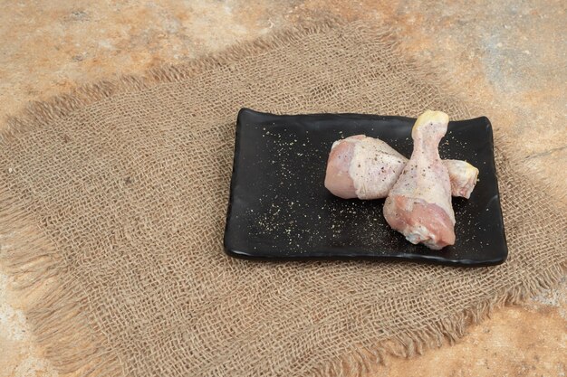 Een donkere plaat van ongekookte kippenpoten met kruiden op een zak