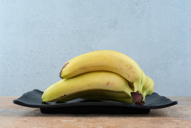 Een donkere plaat vol rijpe fruitbananen op grijs